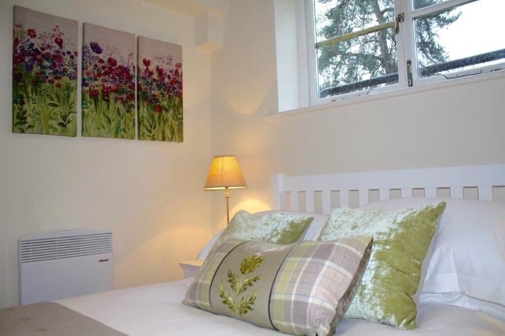 A bedroom with a white bed, green and plaid pillows, a bedside lamp, and three floral paintings on the wall.
