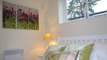 A bedroom with a white bed, green and plaid pillows, a bedside lamp, and three floral paintings on the wall.