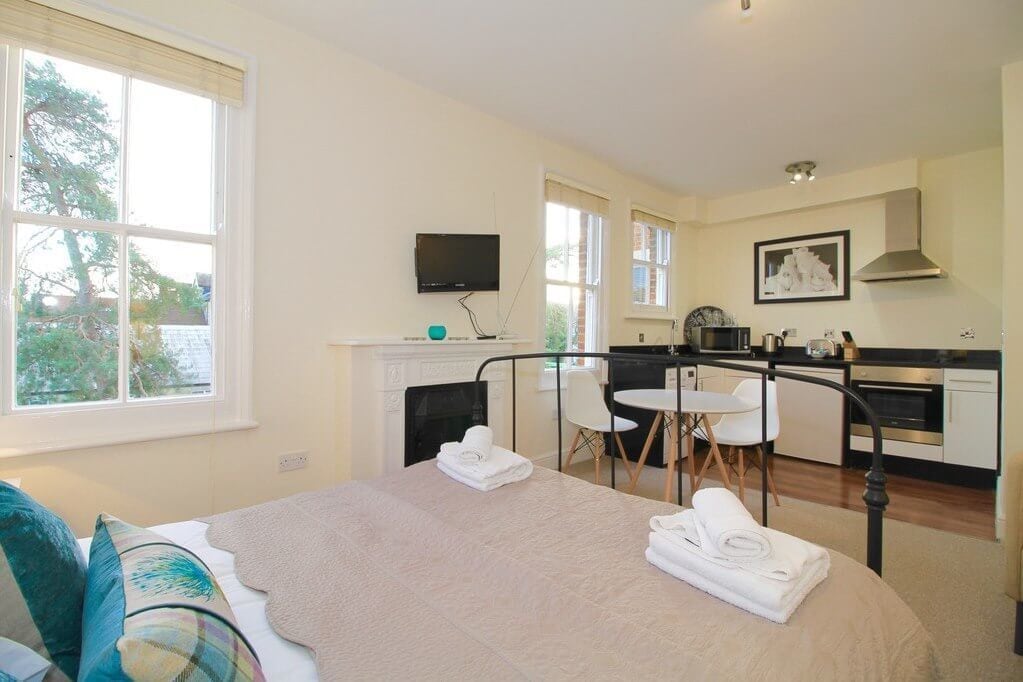 A bedroom with a bed, a desk, and a kitchenette.