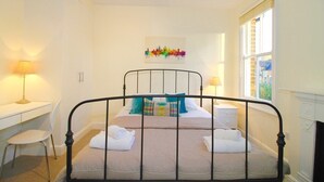 A bedroom with a bed, two bedside tables, a desk, a chair, and a window. - Noa Residence (Oxford)