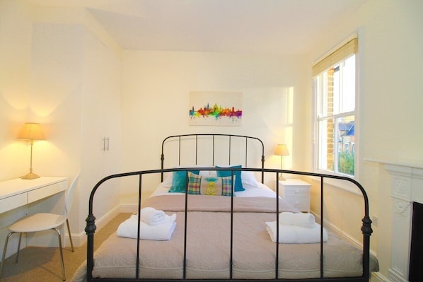 Ein Schlafzimmer mit einem Bett, zwei Nachttischen, einem Schreibtisch, einem Stuhl und einem Fenster.