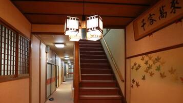 A traditional Japanese interior with a wooden staircase, sliding doors, and a sign with Japanese characters.