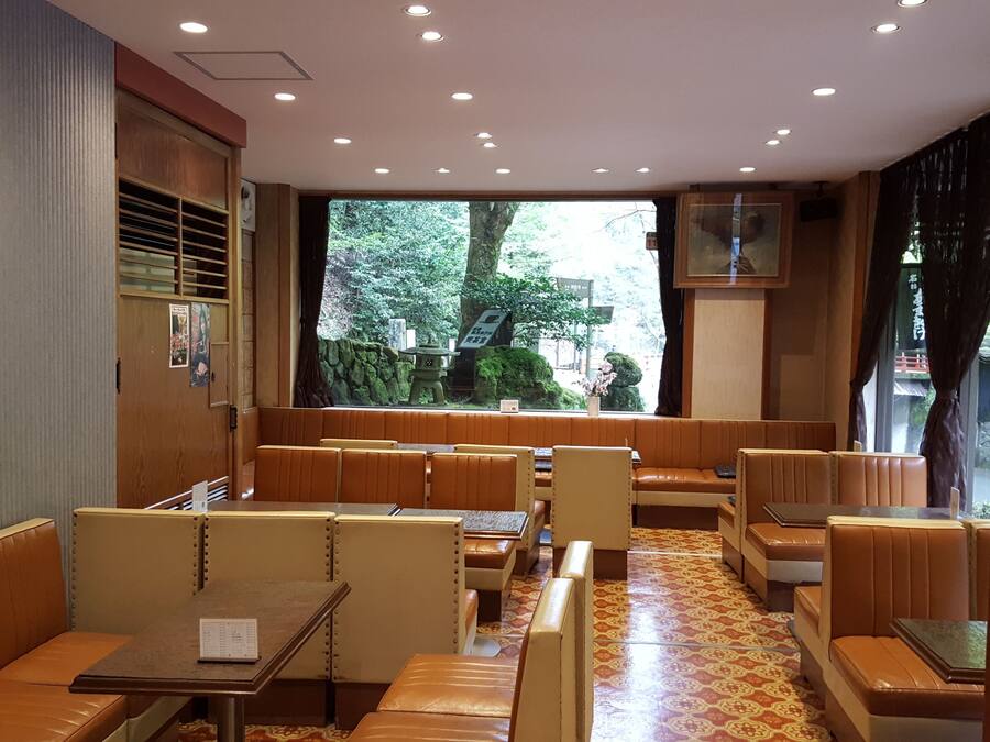 Un restaurante con cabinas y mesas, un suelo estampado y vistas a árboles desde el exterior.