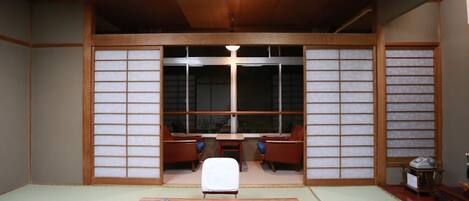 Une pièce avec un sol recouvert de tatamis, une table basse en tatami, une table traditionnelle japonaise et une porte coulissante en papier de riz (shoji).