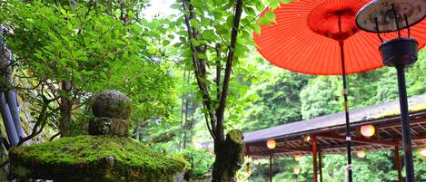 A traditional Japanese garden with a red umbrella, stone lanterns, and a wooden structure in the background.