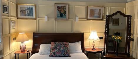 A neatly made bed with a floral pillow, two bedside lamps, a mirror, and framed artwork on the wall.
