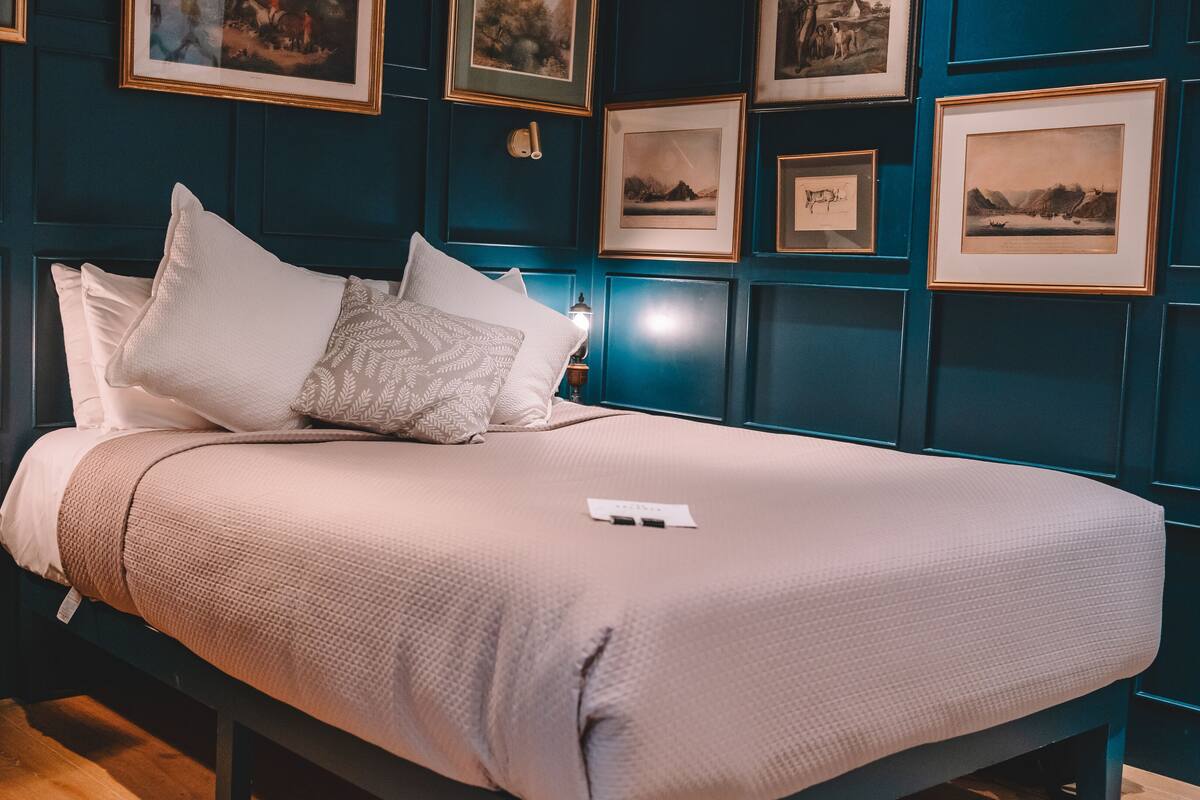 A neatly made bed with a white comforter and several pillows, a bedside table with a lamp, and a wall adorned with framed pictures.