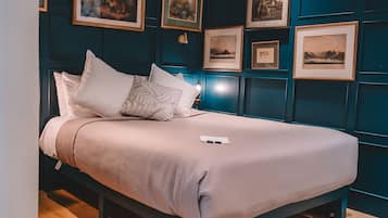 A neatly made bed with a white comforter and several pillows, a bedside table with a lamp, and a wall adorned with framed pictures.