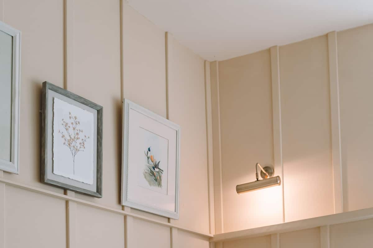 A neatly made bed with white linens and a teal throw blanket, a bedside lamp, and two framed botanical prints on the wall.