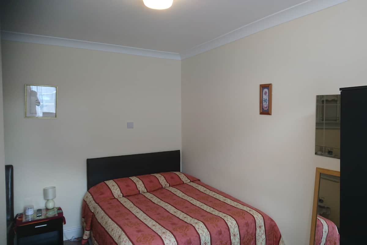 Quarto com cama, mesa de cabeceira, abajur, espelho e guarda-roupa.