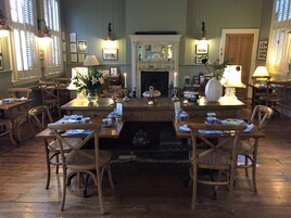 A dining area with wooden tables and chairs, a fireplace, and wall-mounted lamps.