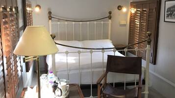 A hotel room with a single bed, a wooden chair, a table with a lamp, and a tray with a cup and saucer.
