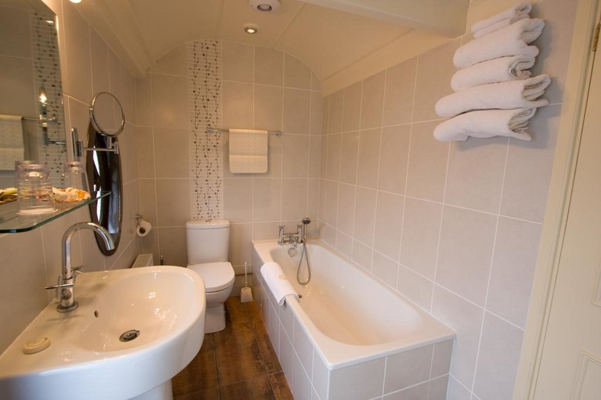 A modern bathroom with a sink, toilet, and bathtub. There are towels hanging on the wall and a glass shelf with toiletries.