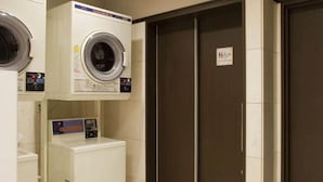A laundry room with a front-loading washer and dryer, a small refrigerator, and a pair of closed double doors.