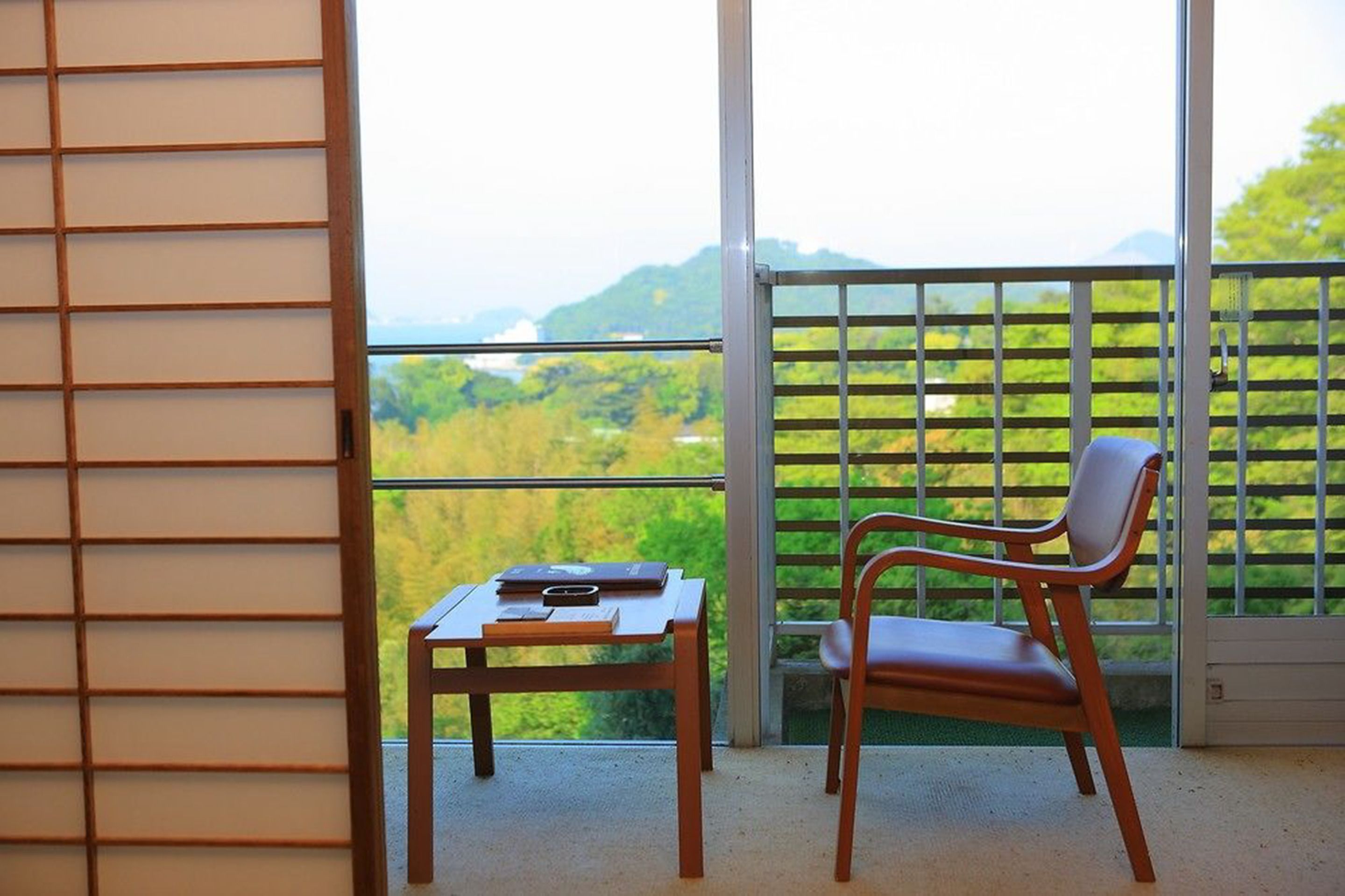 Un balcón con vista a un paisaje verde, una mesa de madera y una silla.