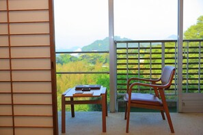 A balcony with a view of a green landscape, a wooden table, and a chair. - Senpokaku (Toba)
