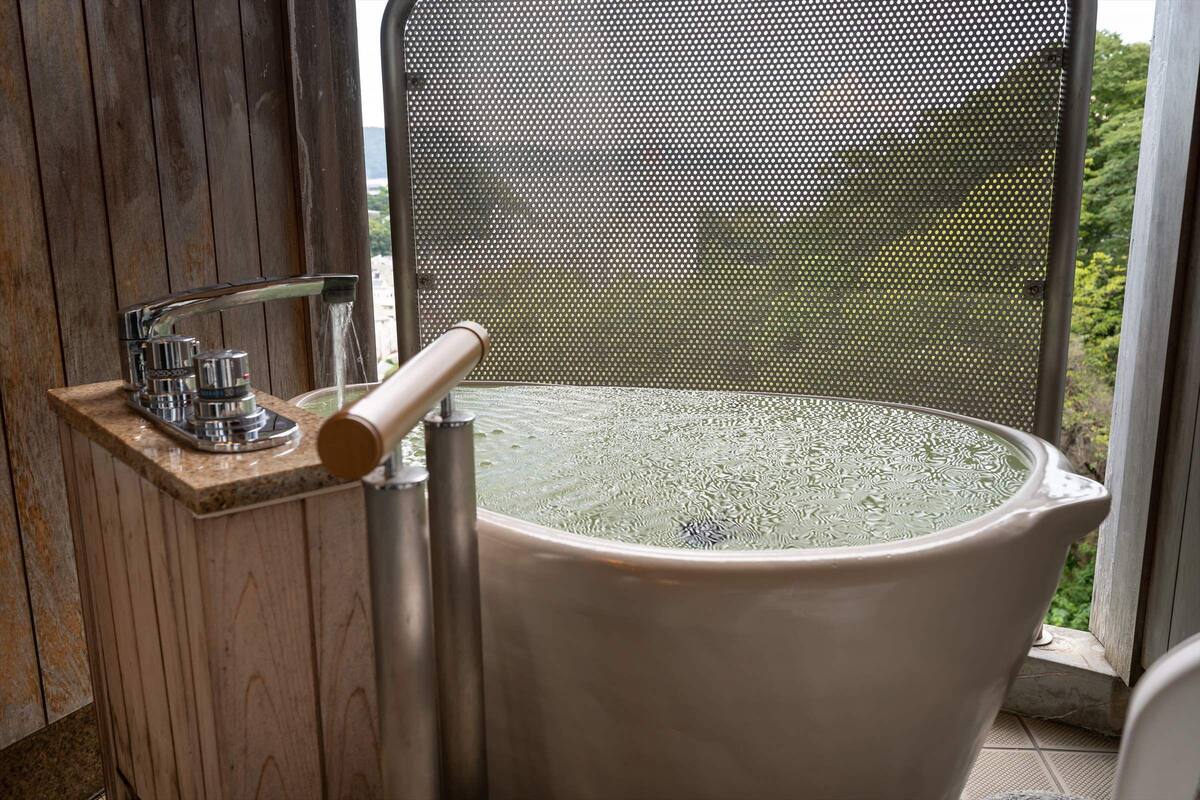 A bathroom with a large bathtub, a shower area, and a window with a view of greenery.