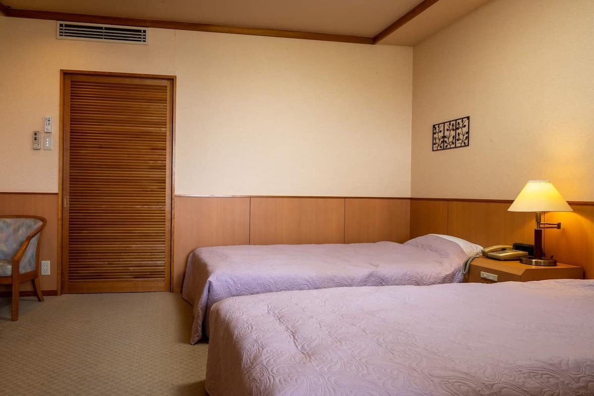 Habitación de hotel con dos camas, una silla, un escritorio, una lámpara y un teléfono instalado en la pared.