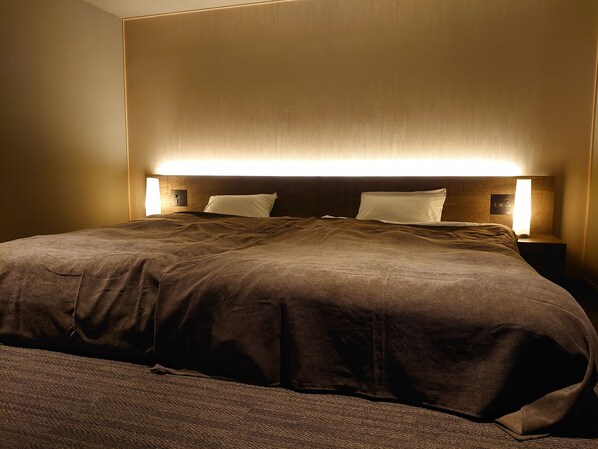 A neatly made bed with a dark brown blanket and two pillows, flanked by wall-mounted nightstands with lamps. - Senpokaku (Toba)