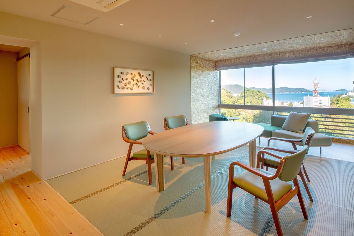 A conference room with a large table and chairs, a framed artwork on the wall, and a view of a cityscape through large windows.