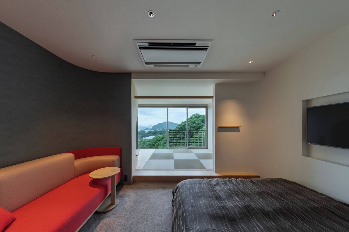 A modern bedroom with a large bed, a red sofa, a small table, and a TV mounted on the wall.