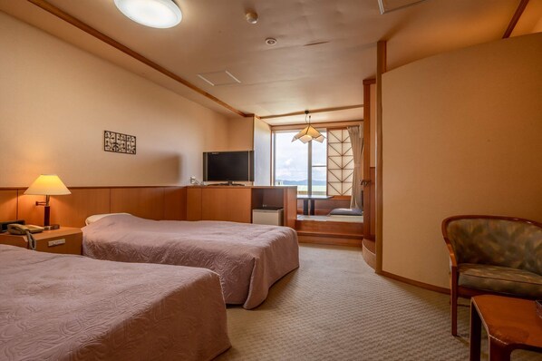 Habitación de hotel con dos camas, televisión, escritorio, lámpara y vistas al exterior.