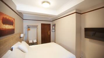 A hotel room with a large bed, a wooden headboard, a flat-screen TV mounted on the wall, and a ceiling light.
