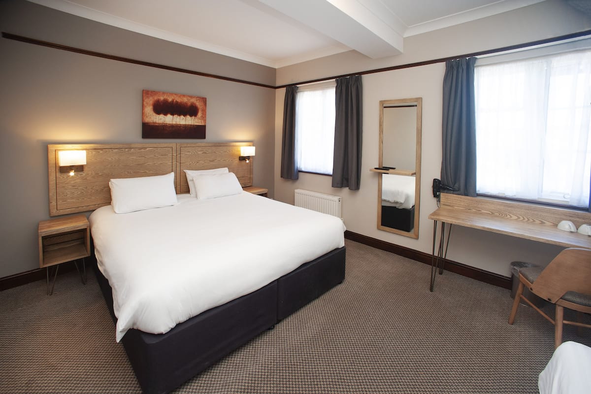 A hotel room with a large bed, a desk, a mirror, and a painting on the wall.