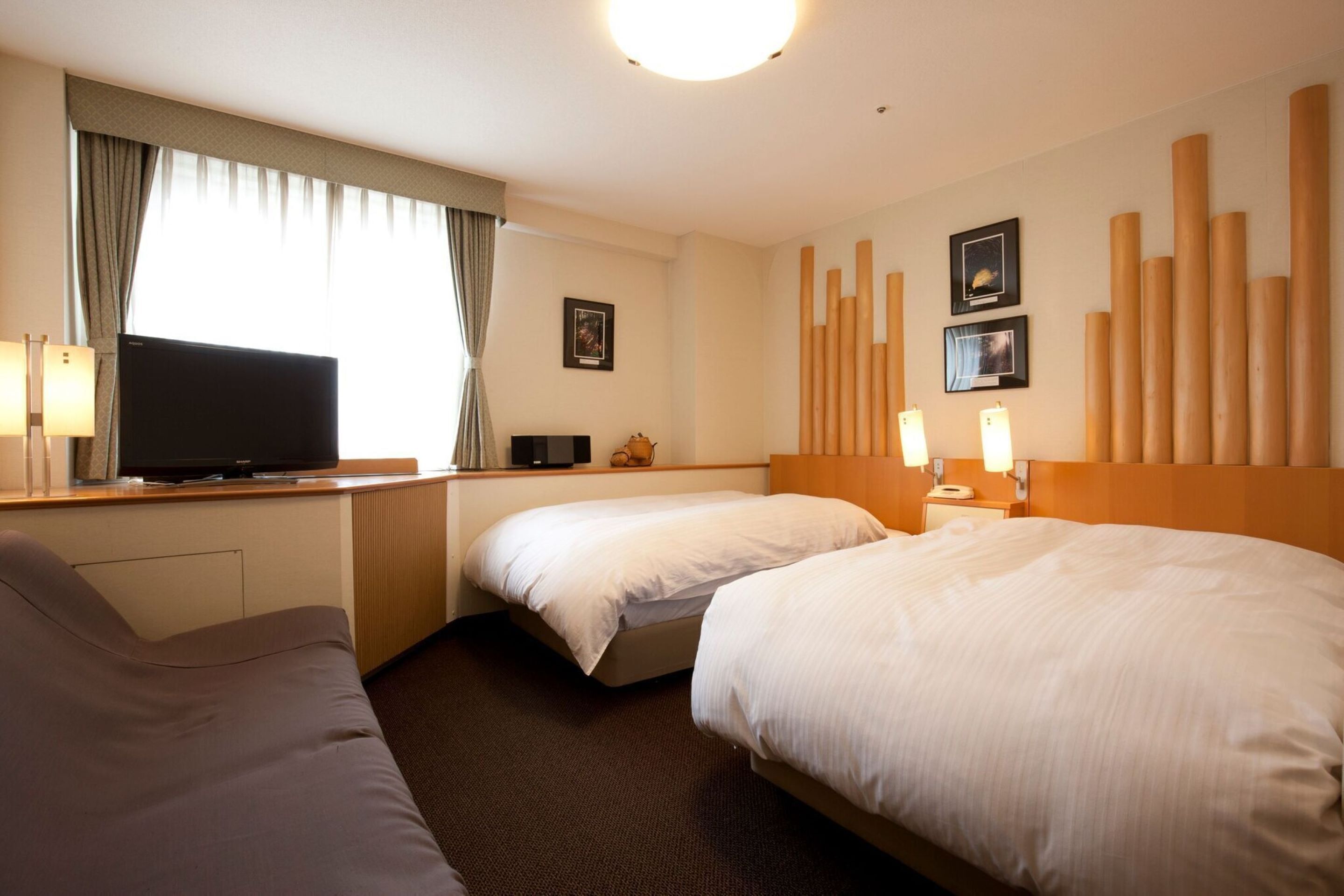 Une chambre d’hôtel avec deux lits, un canapé, une télévision et une grande fenêtre avec des rideaux.