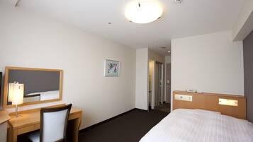 Quarto de hotel com cama, escrivaninha, cadeira e espelho.