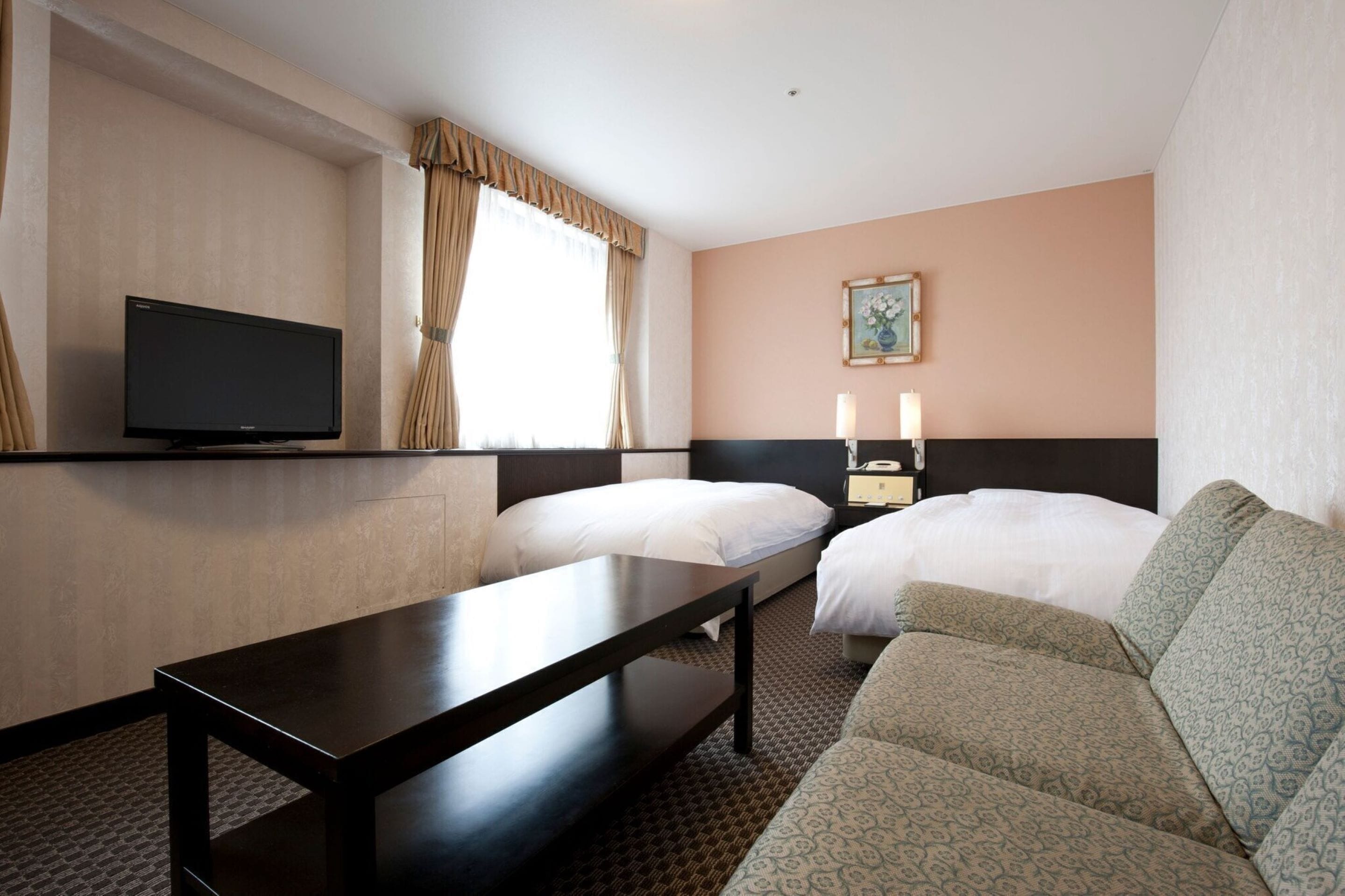 A hotel room with two beds, a TV, a bedside table, a sofa, and a painting on the wall.