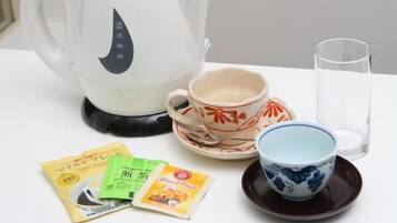 A white kettle, two cups, a glass, and tea packets on a white table.