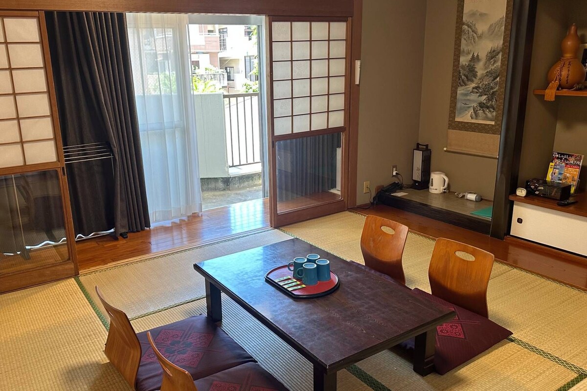 A traditional Japanese room with tatami flooring, a low table with a tray of cups, and a sliding door leading to an outdoor area.