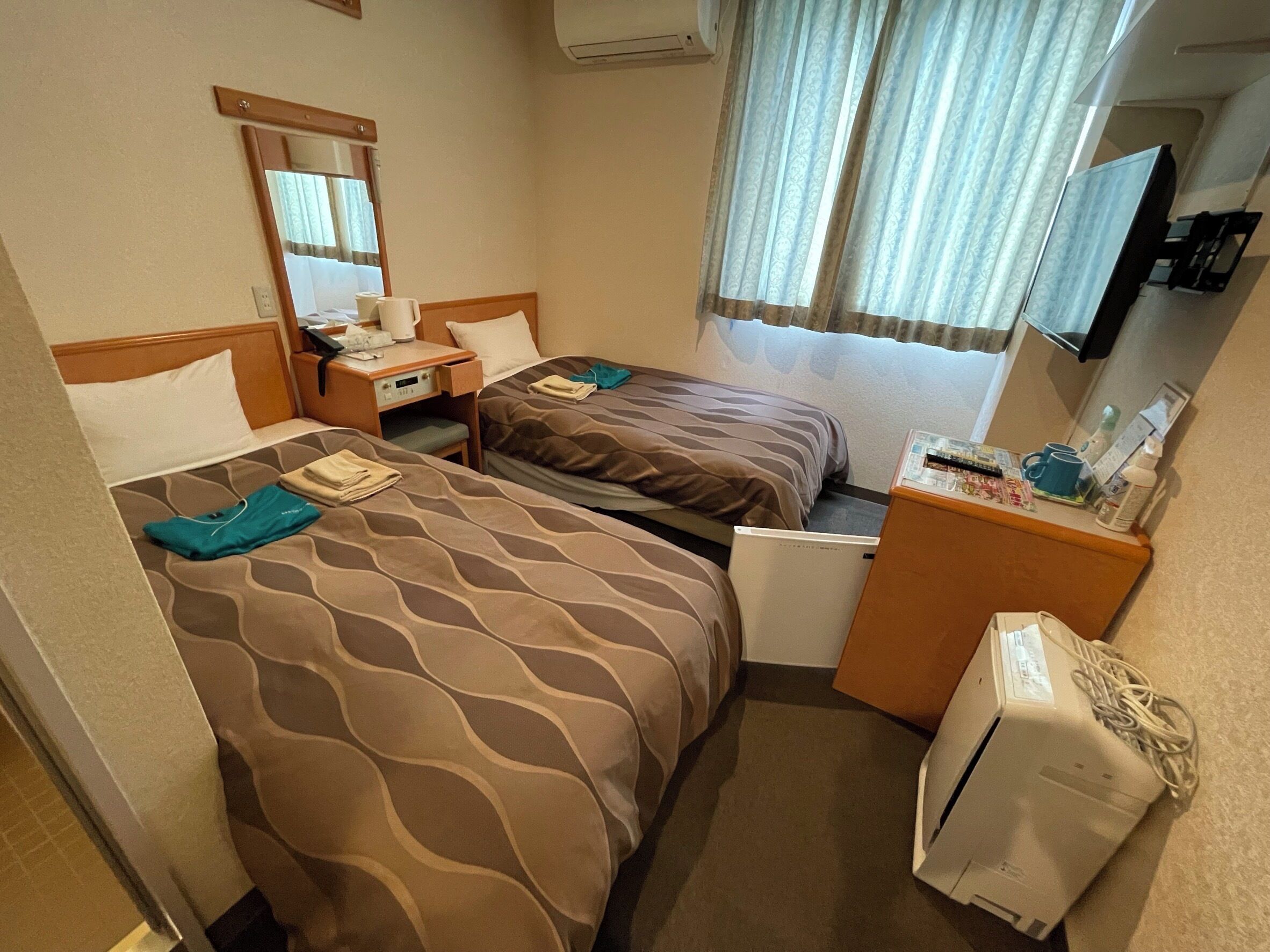 A hotel room with two beds, a desk, a mirror, a television, and a minibar.