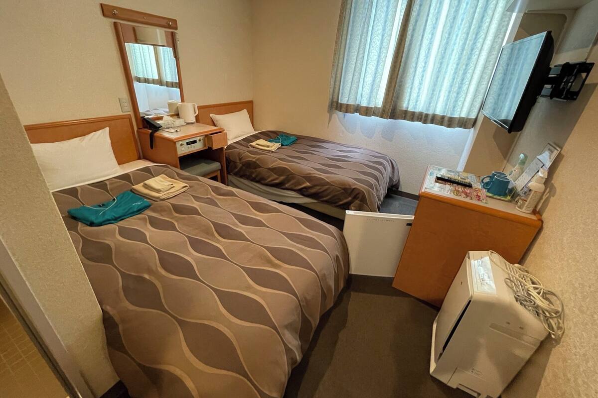 Hotellihuone, jossa on kaksi sänkyä, työpöytä, peili, televisio ja minibaari.