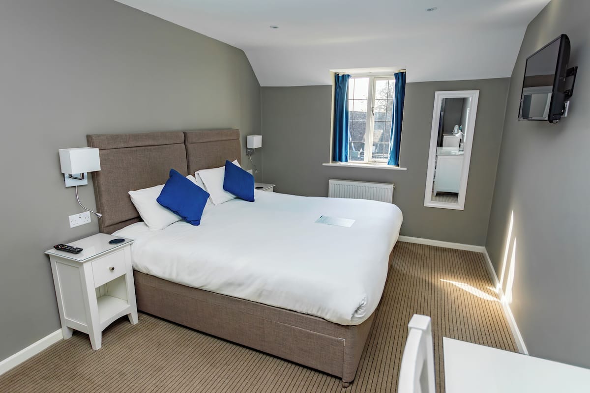A neatly arranged hotel room with a large bed, bedside tables, a window with curtains, a mirror, and a flat-screen TV mounted on the wall.