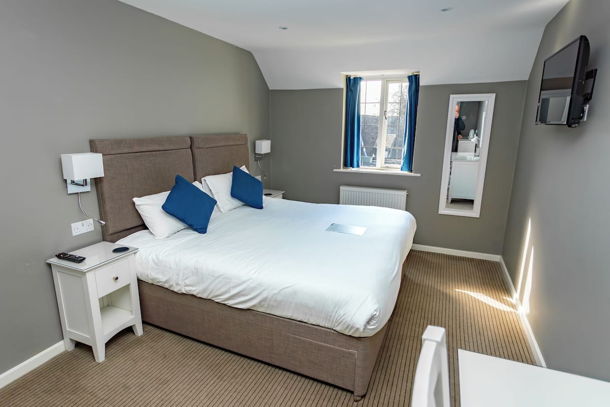 A neatly arranged hotel room with a large bed, bedside tables, a window with curtains, a mirror, and a television mounted on the wall.