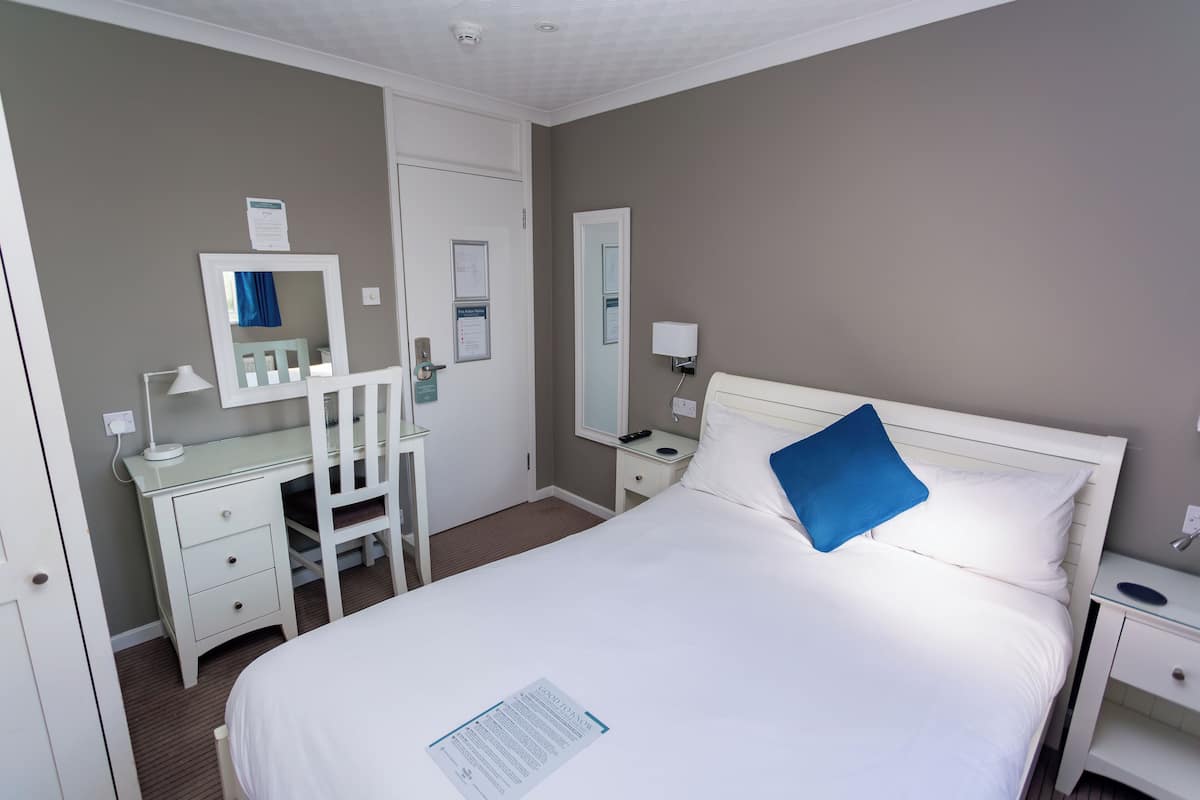 A hotel room with a bed, a desk, a chair, a mirror, and a nightstand.