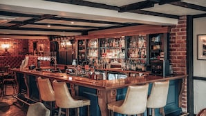 Un bar con mostrador de madera, taburetes de cuero y pared de ladrillo.