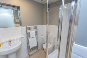 A modern bathroom with a white sink, a glass-enclosed shower, and a toilet.