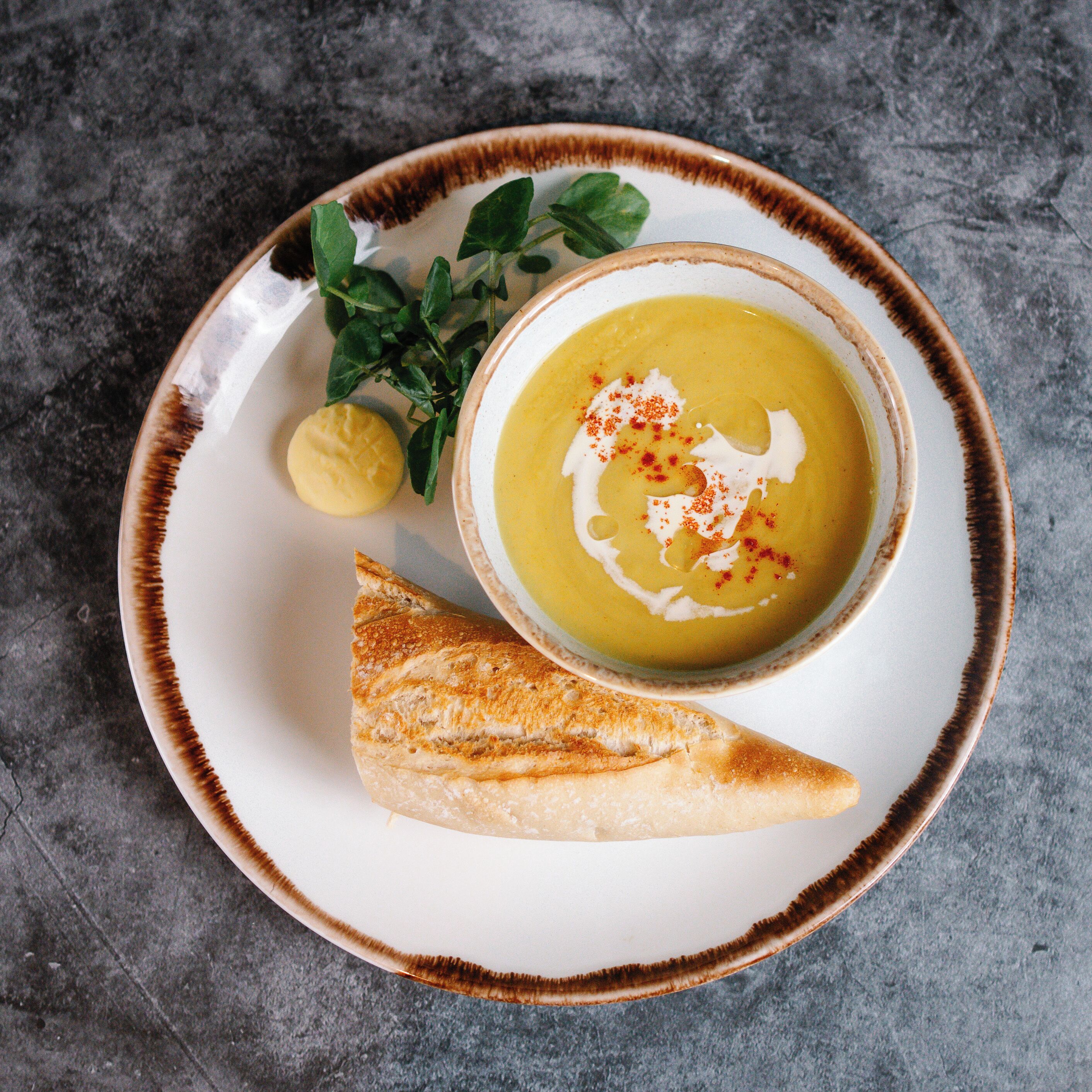 Un bol de soupe agrémenté d’une garniture, une tranche de pain et un quartier de citron sur une assiette.