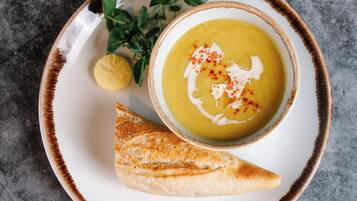Un bol de soupe agrémenté d’une garniture, une tranche de pain et un quartier de citron sur une assiette.
