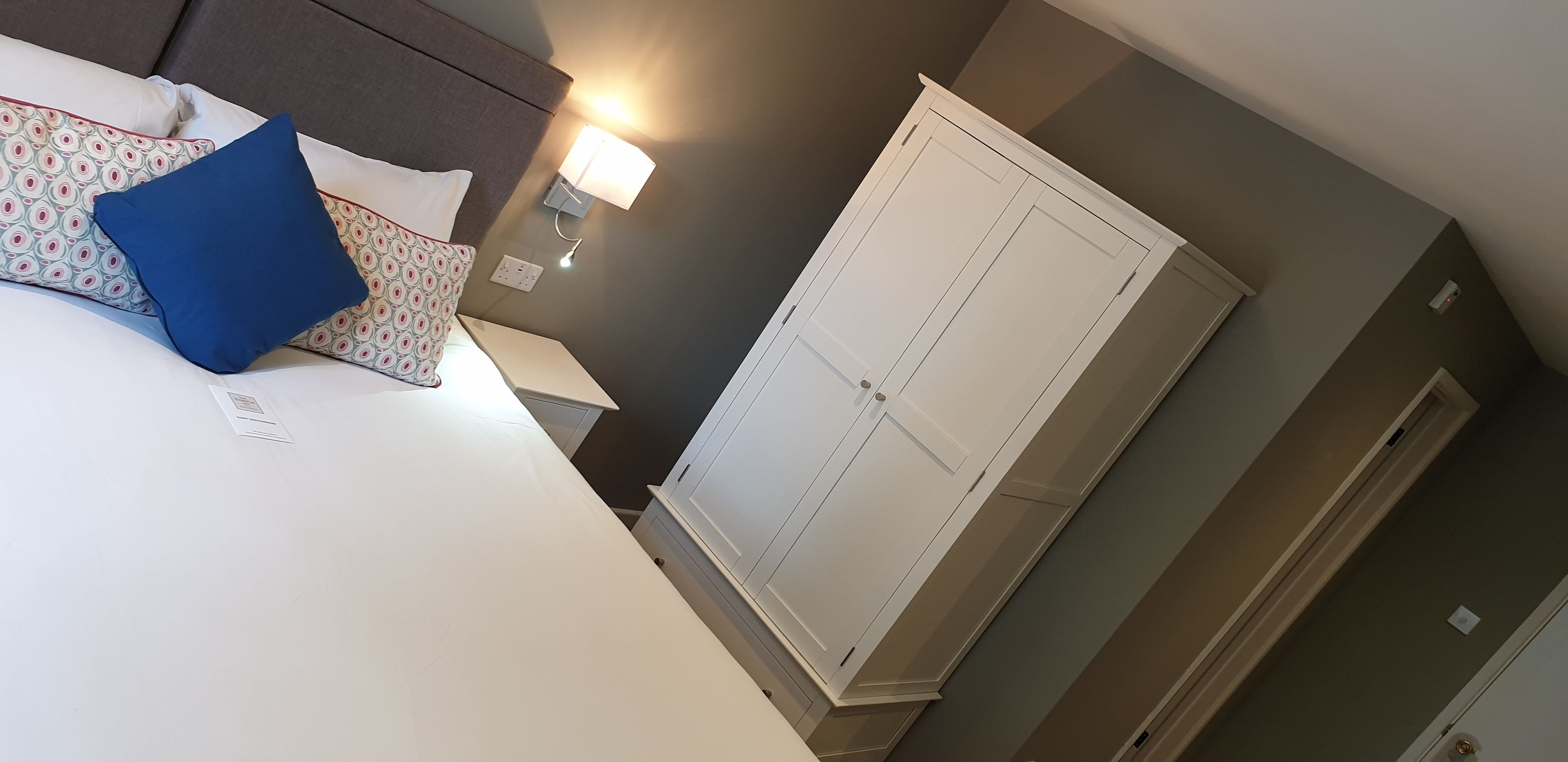 Un dormitorio con cama, almohadas, una mesita de noche, una lámpara y un armario.