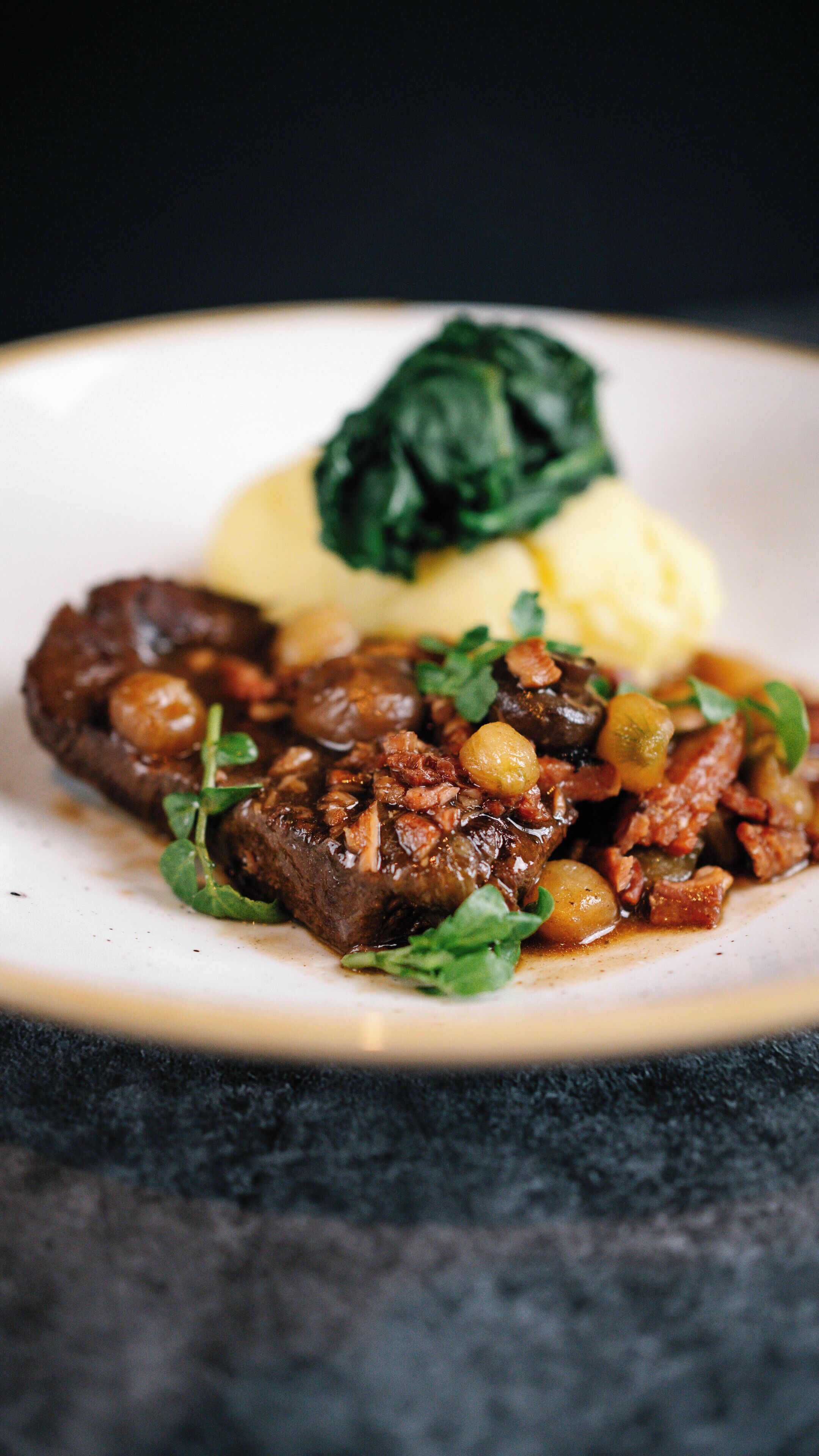 A plate with a beef dish, mashed potatoes, and spinach.