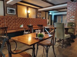 A cozy restaurant with wooden tables and chairs, a cushioned bench area, and brick walls.