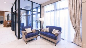 A modern hotel room with two sofas, a glass partition, and large windows with curtains.