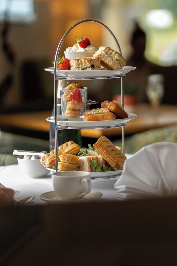 Un soporte de tres niveles para postres con diversas pastelerías y una taza de té sobre una mesa.