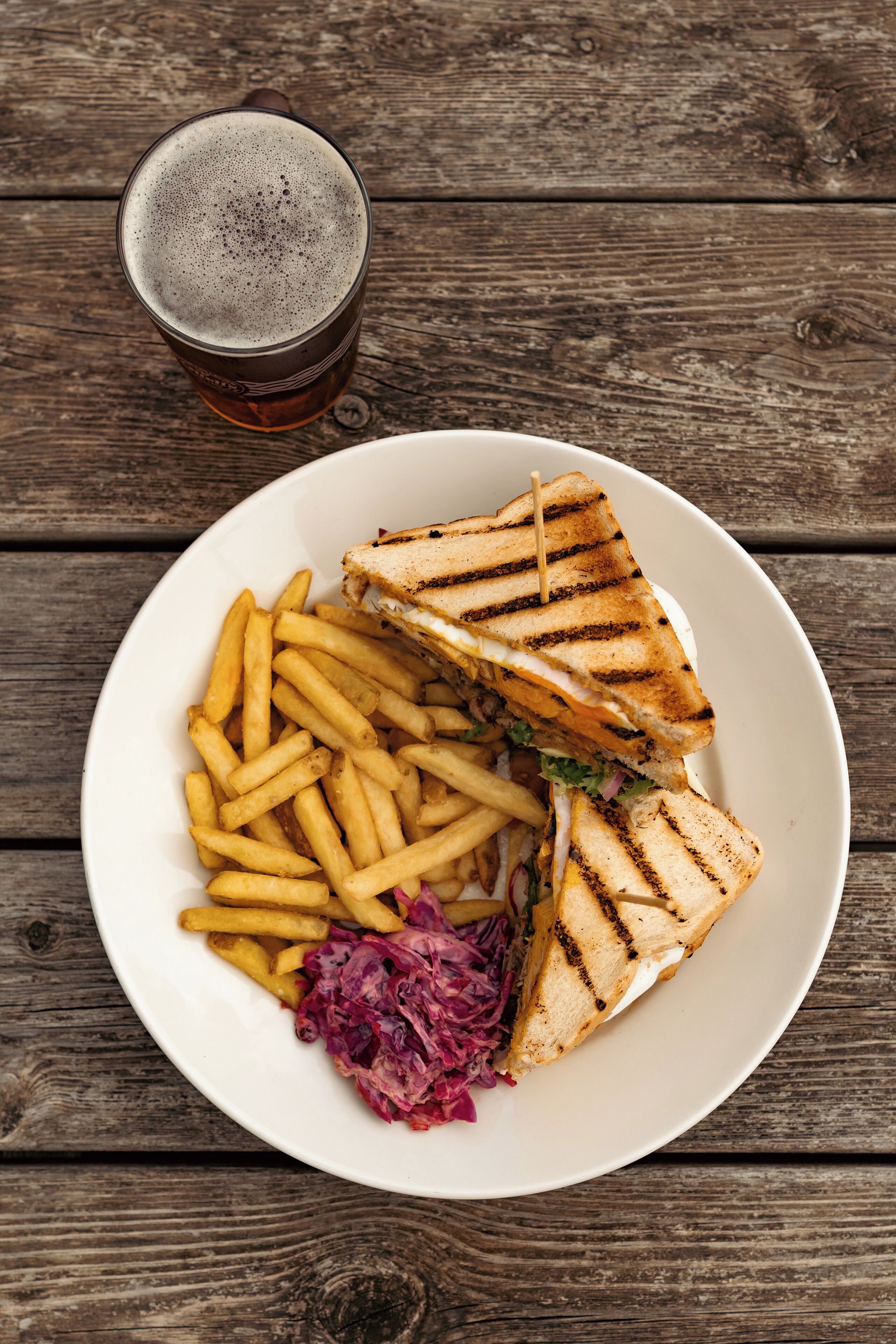 A plate with a grilled sandwich, French fries, and sauerkraut on a wooden table.