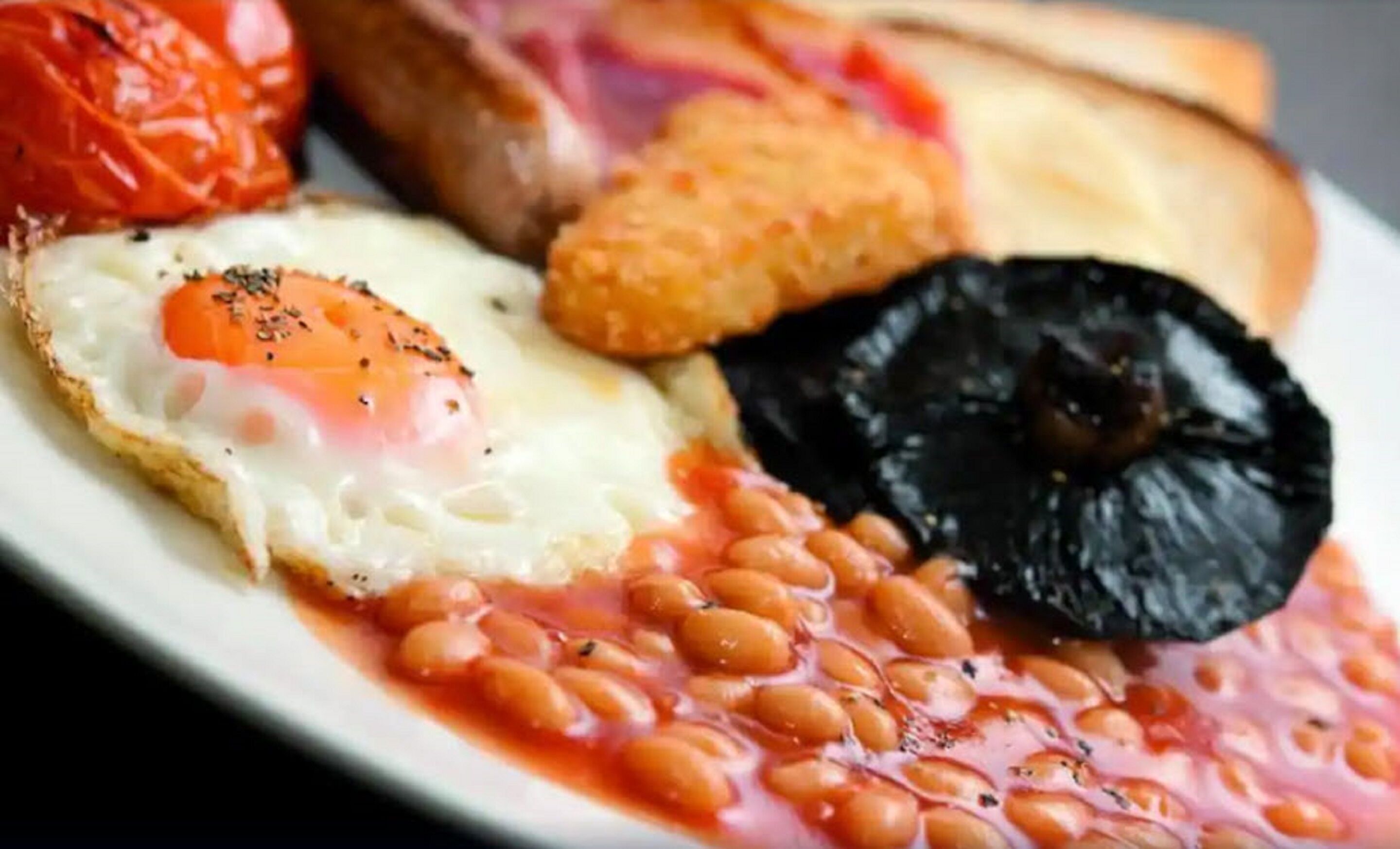 A plate with a fried egg, baked beans, a slice of black pudding, a tomato, and a piece of toast.