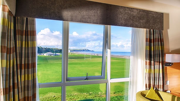 A room with a large window offering a view of a green field and a beach.